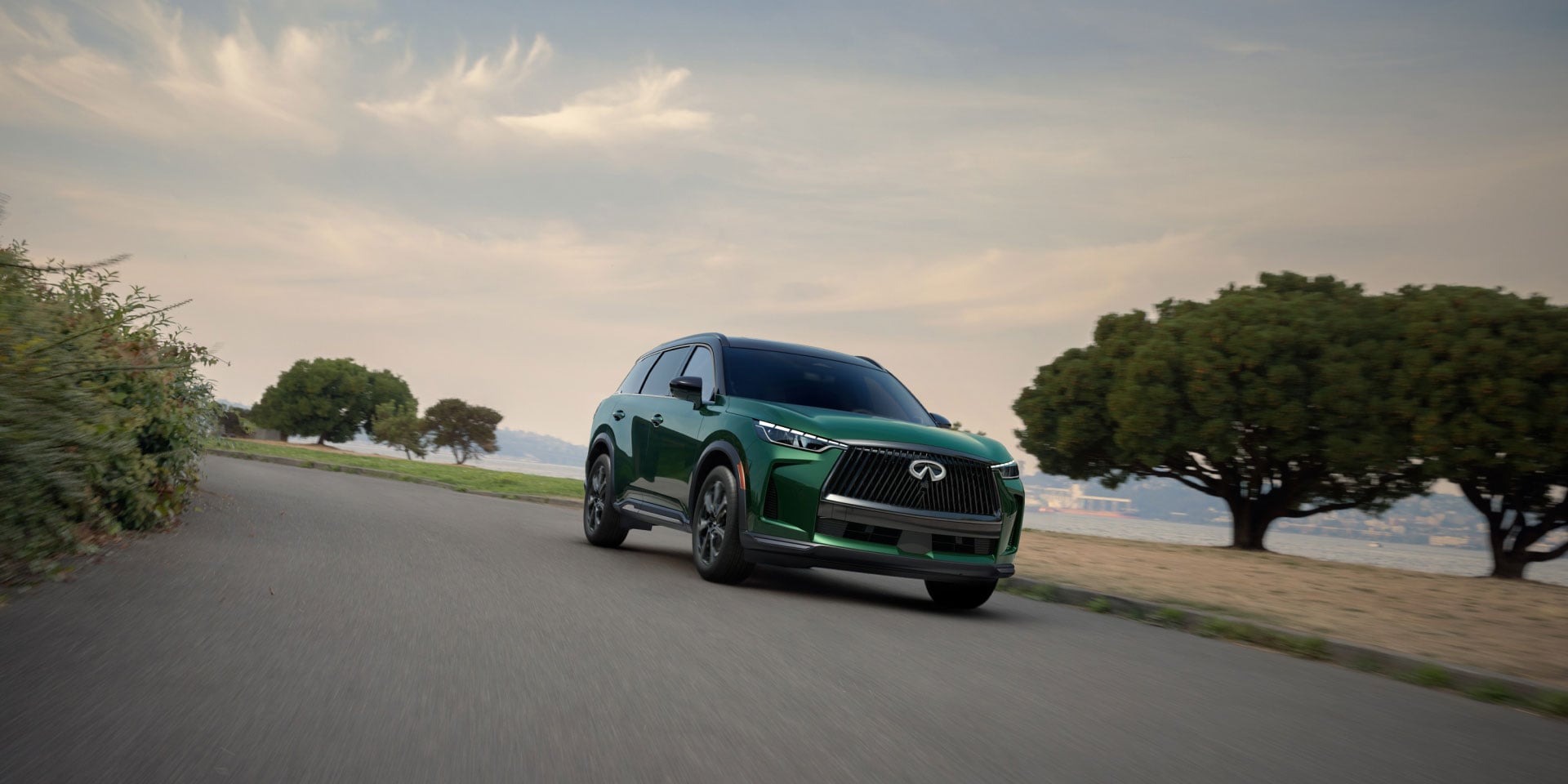 A front view of a green INFINITI QX60 driving around a slight curve in the road