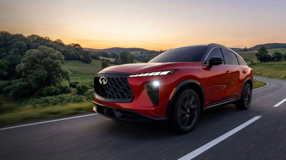 A red 2027 INFINITI QX65 SUV driving down a curving road at sunrise